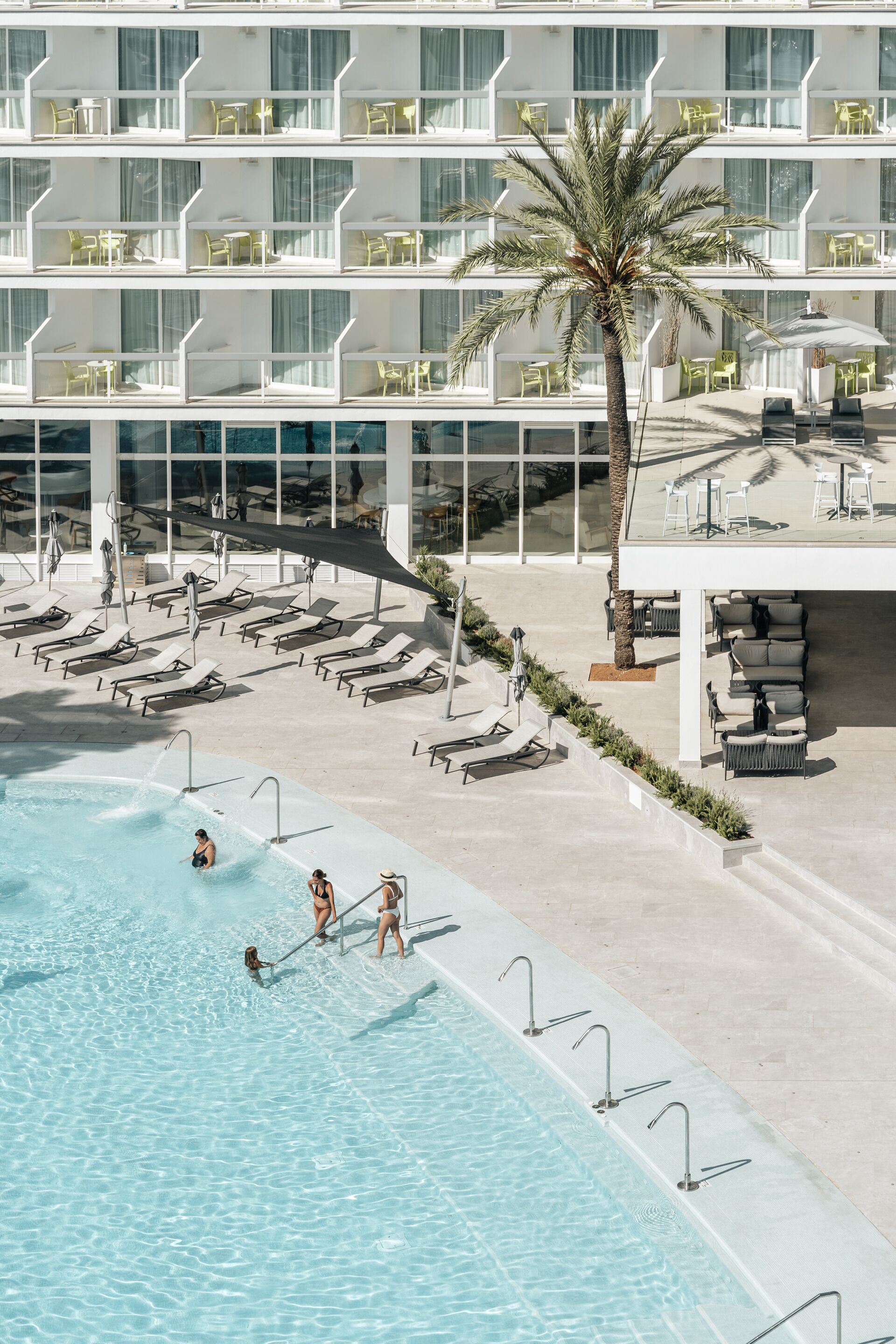 A hotel with a pool area, sun loungers, and a palm tree.