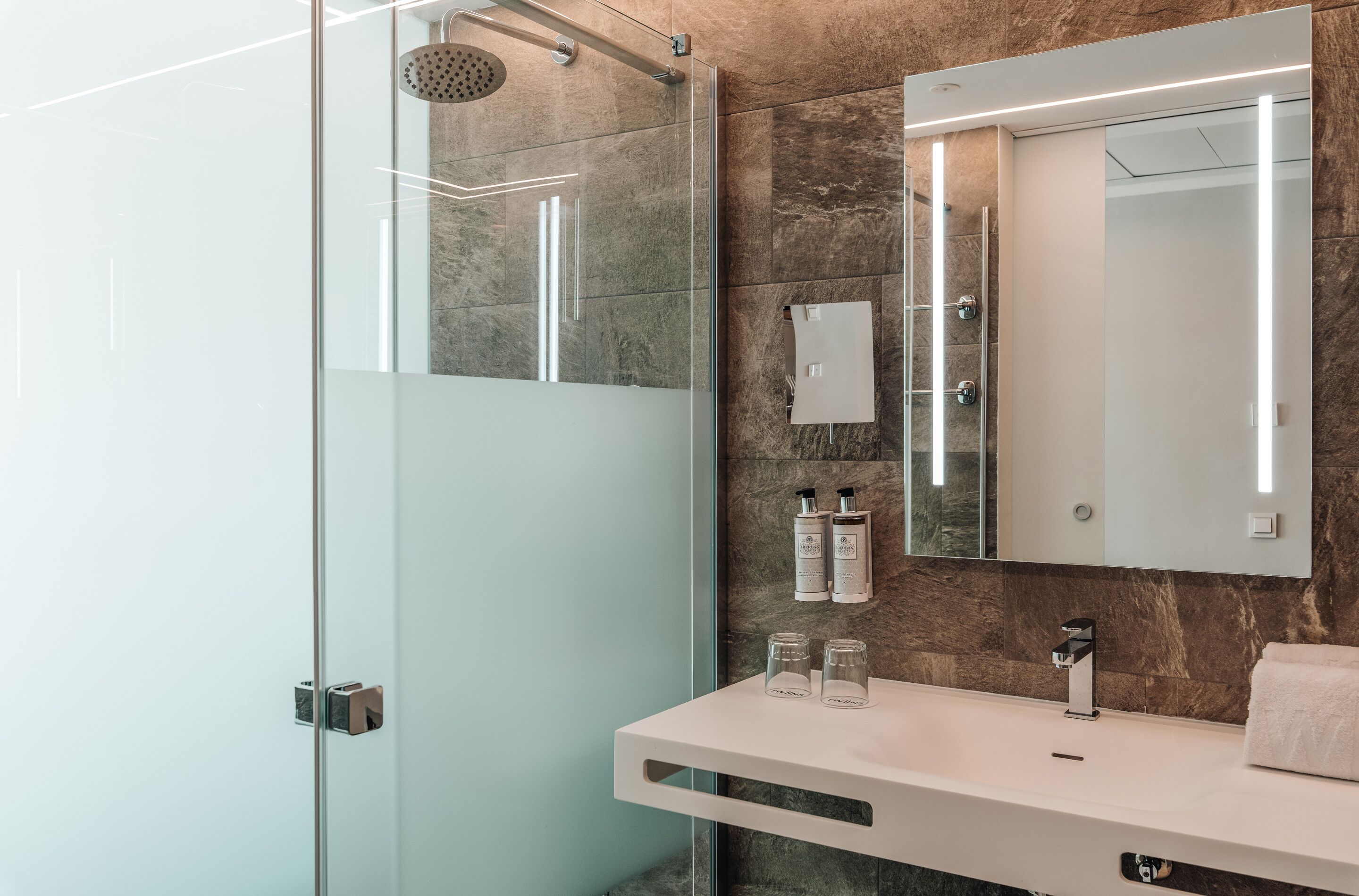 Ein modernes Badezimmer mit einer gläsernen Duschkabine, einem weißen Waschtisch mit Spiegel und Pflegeprodukten an der Wand.