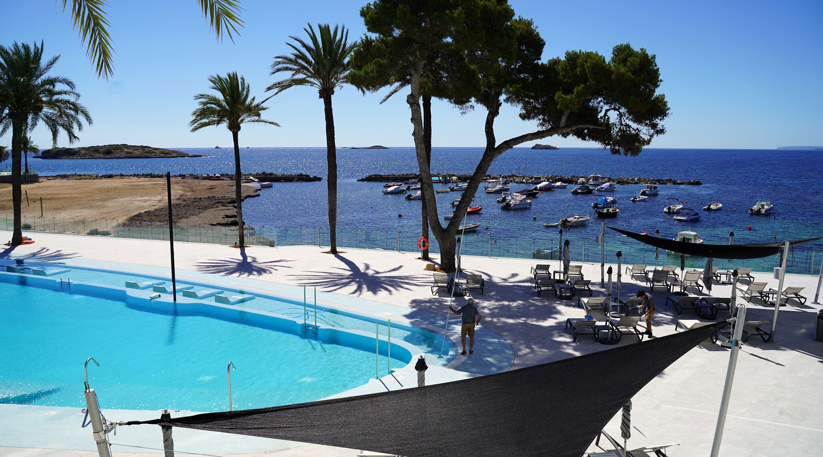 Un espace piscine doté de chaises longues et de parasols, avec vue sur une marina où sont amarrés des bateaux.