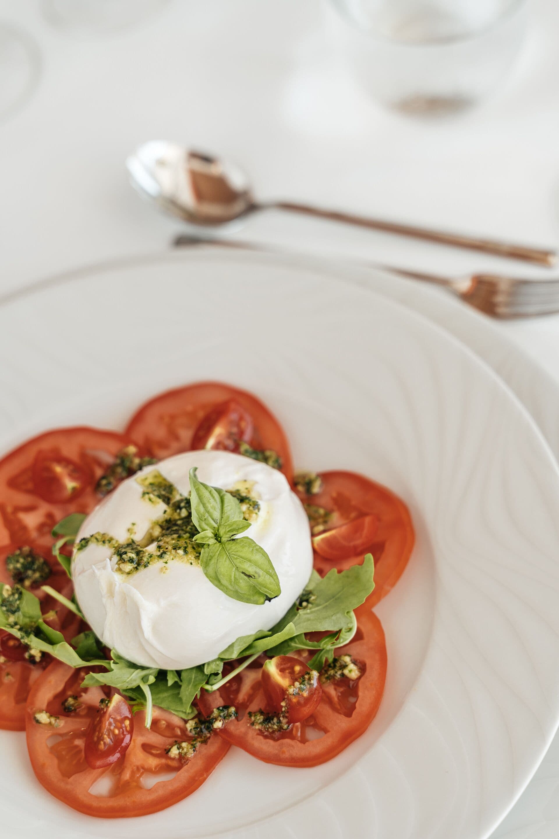 A white plate with a salad of tomato slices, basil, and a dollop of cream.