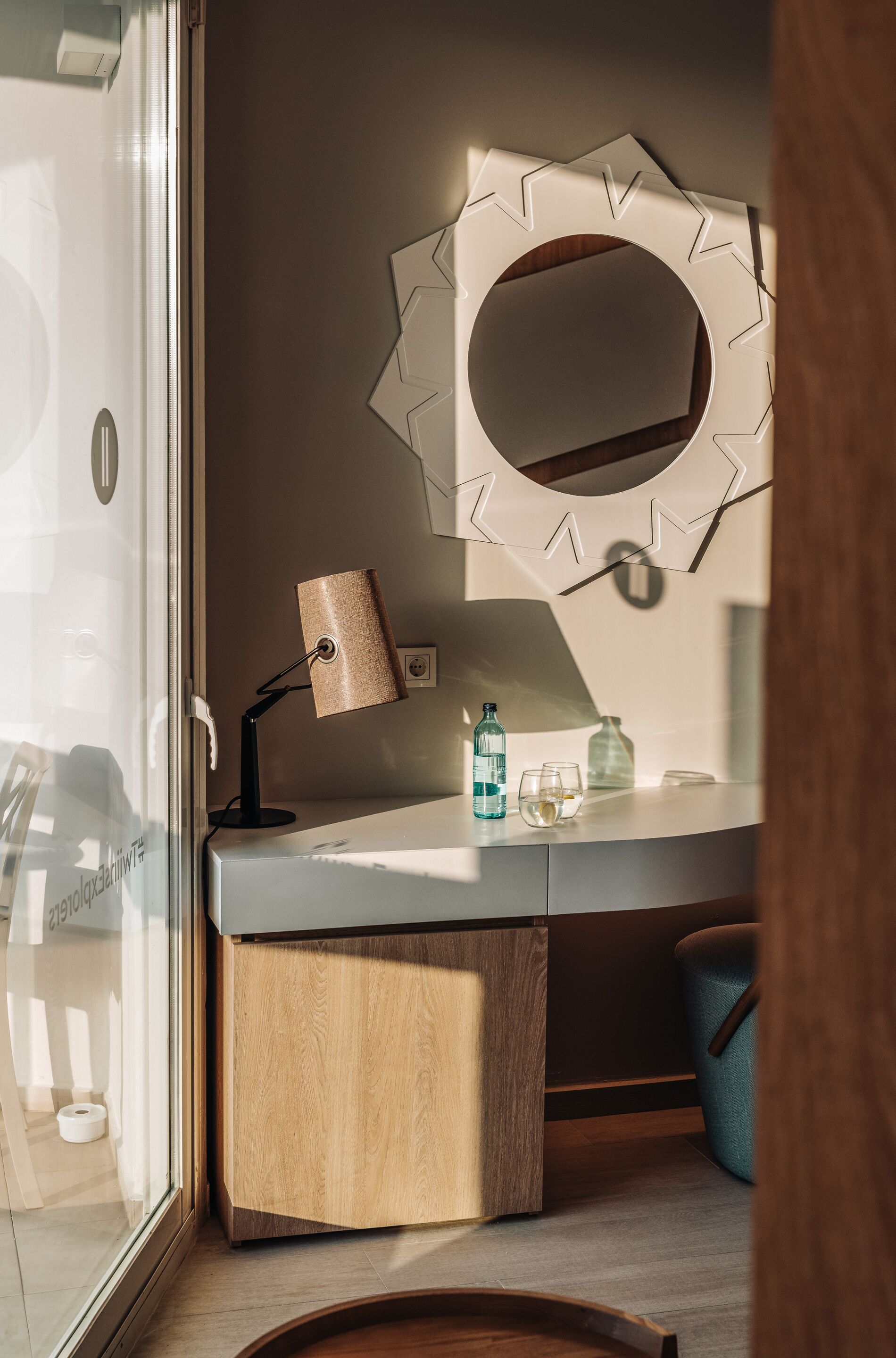 Et moderne badeværelse med en trækommode, et spejl med geometrisk ramme, en lampe og en glasbrusekabine.