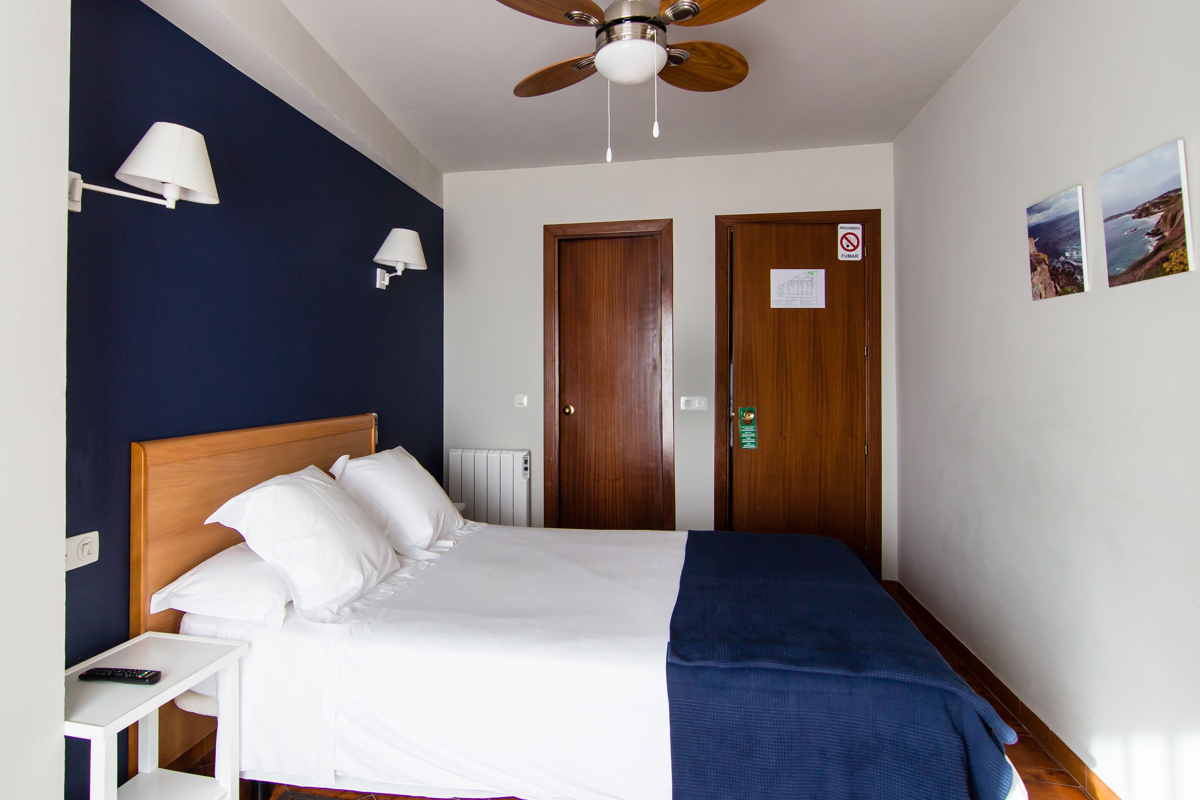Ein Hotelzimmer mit einem Bett, einem Deckenventilator, zwei Türen, einem Nachttisch und einer Wandlampe.