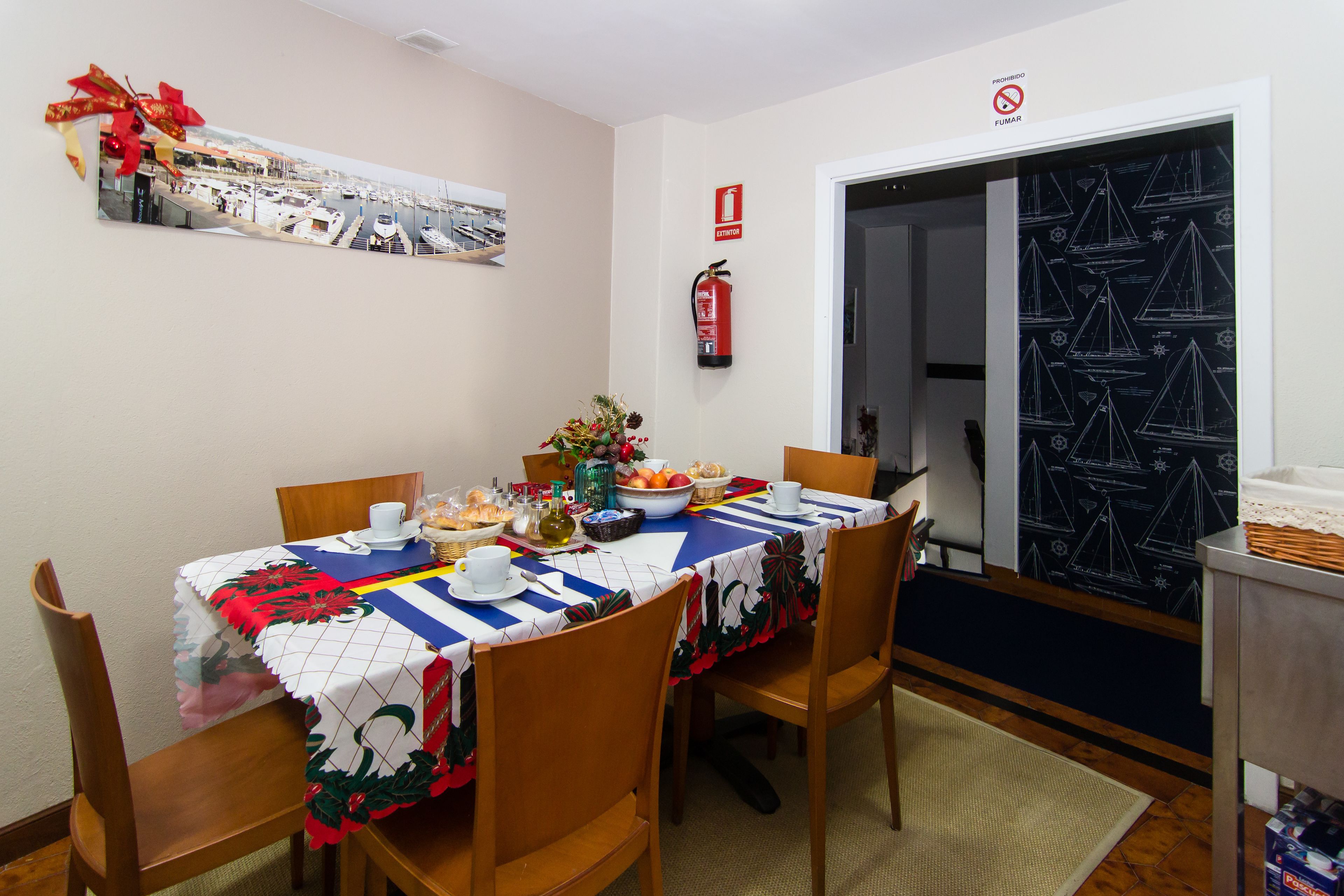 Un comedor con una mesa dispuesta para comer, sillas, un extintor y una puerta con cortina de temática náutica.