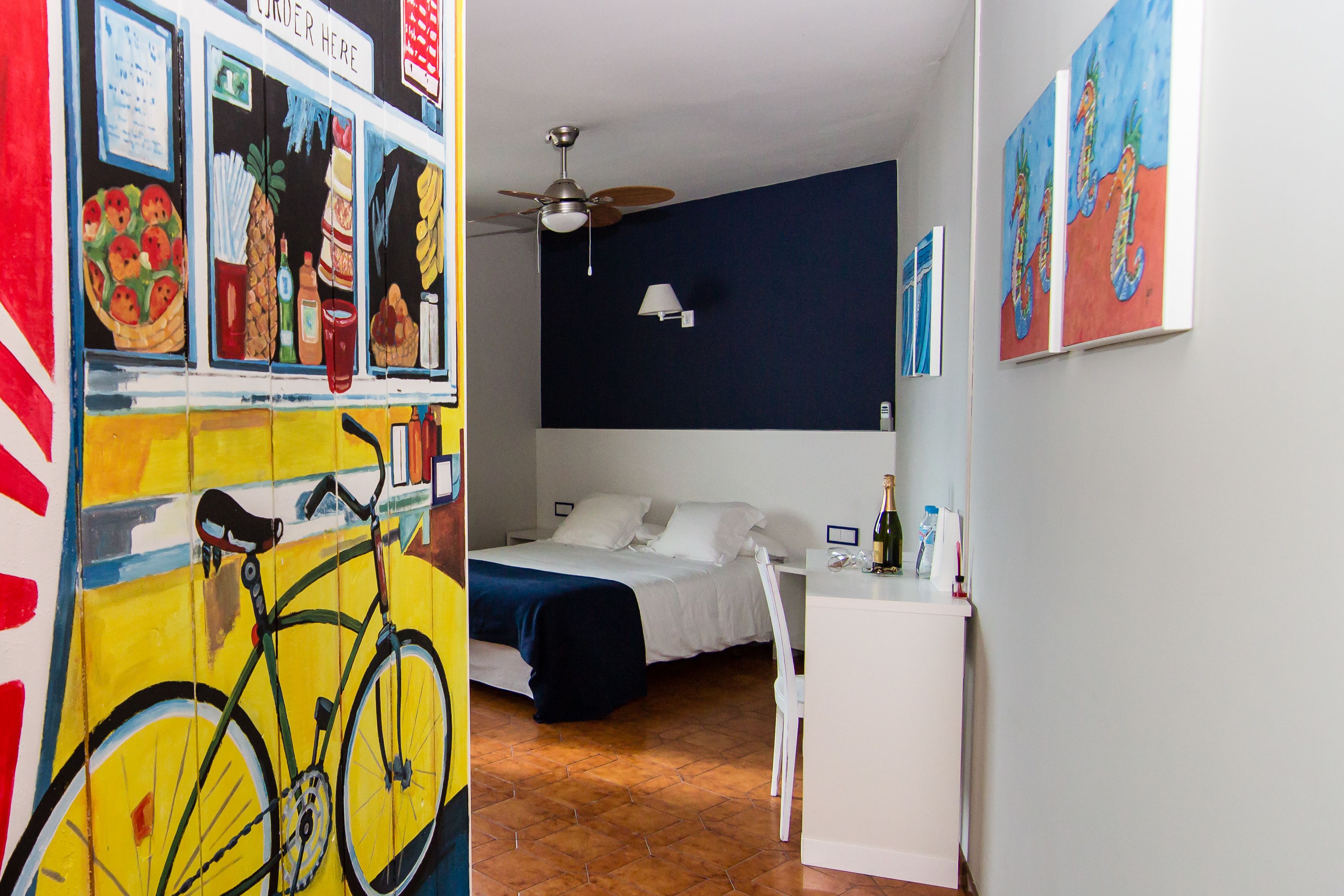 Ein Zimmer mit einem Bett, einem Schreibtisch, einem Fahrrad und einer Wand mit einem Wandgemälde.