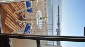 Een zonnig buitenterrein met een tafel, stoelen, een fles water en uitzicht op het strand en de zee.