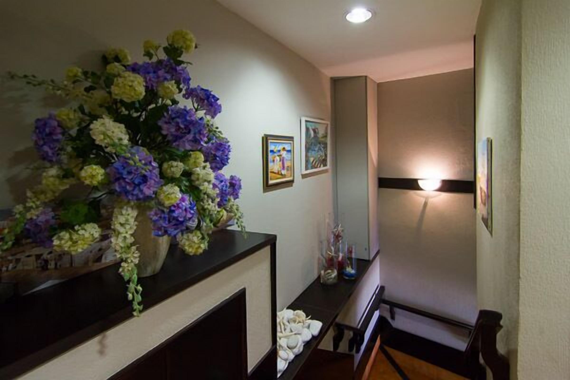 Un pasillo con un arreglo floral sobre un mostrador, cuadros en la pared y una lámpara.
