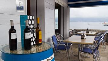 A dining area with a table and chairs, a wine display with bottles, and a view of the sea.