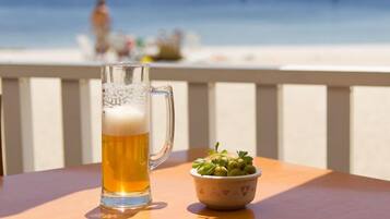 A beer mug on a table with a bowl of olives and a view of the beach in the background.