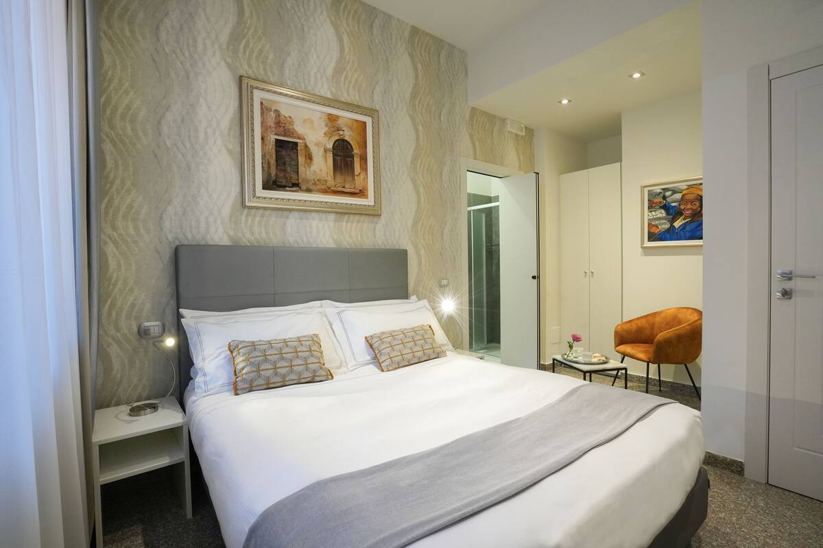 A neatly made bed with a grey headboard, a bedside table with a lamp, and a framed picture on the wall.