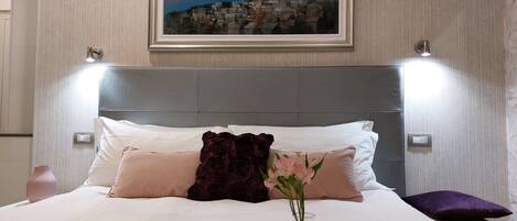 A neatly made bed with a cityscape painting above it, a bedside table with a vase of flowers, and a tray with cups and saucers.