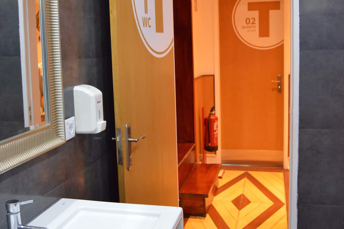 A modern bathroom with a white sink, a mirror, and a door leading to a restroom marked with a 'WC' sign.