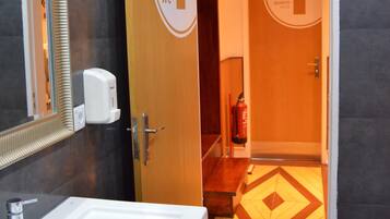 A modern bathroom with a white sink, a mirror, and a door leading to a restroom marked with a 'WC' sign.