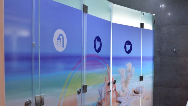 A restroom with glass partitions, a beach mural, and icons indicating amenities. - Terrace Lisbon Hostel (Lisbon)