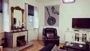 A living room with a fireplace, a black leather armchair, a sofa, a television, and a decorative wall hanging. - Terrace Lisbon Hostel (Lisbon)
