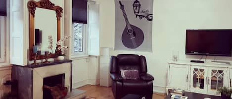 Un salón con chimenea, un sillón de cuero negro, un sofá, un televisor y un adorno de pared.