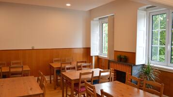 A dining area with wooden tables and chairs, a fireplace, and windows with a view of greenery.
