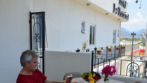 Un hombre leyendo un libro en una mesa redonda sobre un suelo de baldosas, con un vaso de zumo de naranja y un bol de fruta.
