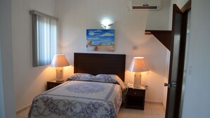 Un dormitorio con una cama, dos mesitas de noche con lámparas, un cuadro en la pared y una puerta.
