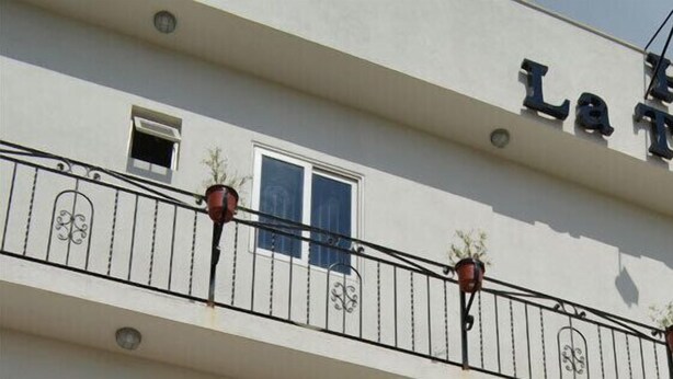 Un hotel llamado "La Terminal" con fachada blanca, señalización negra y un balcón con plantas en macetas.