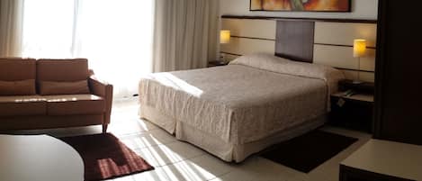 Una habitación de hotel con una cama, un escritorio con lámpara, una silla y una pequeña mesa.