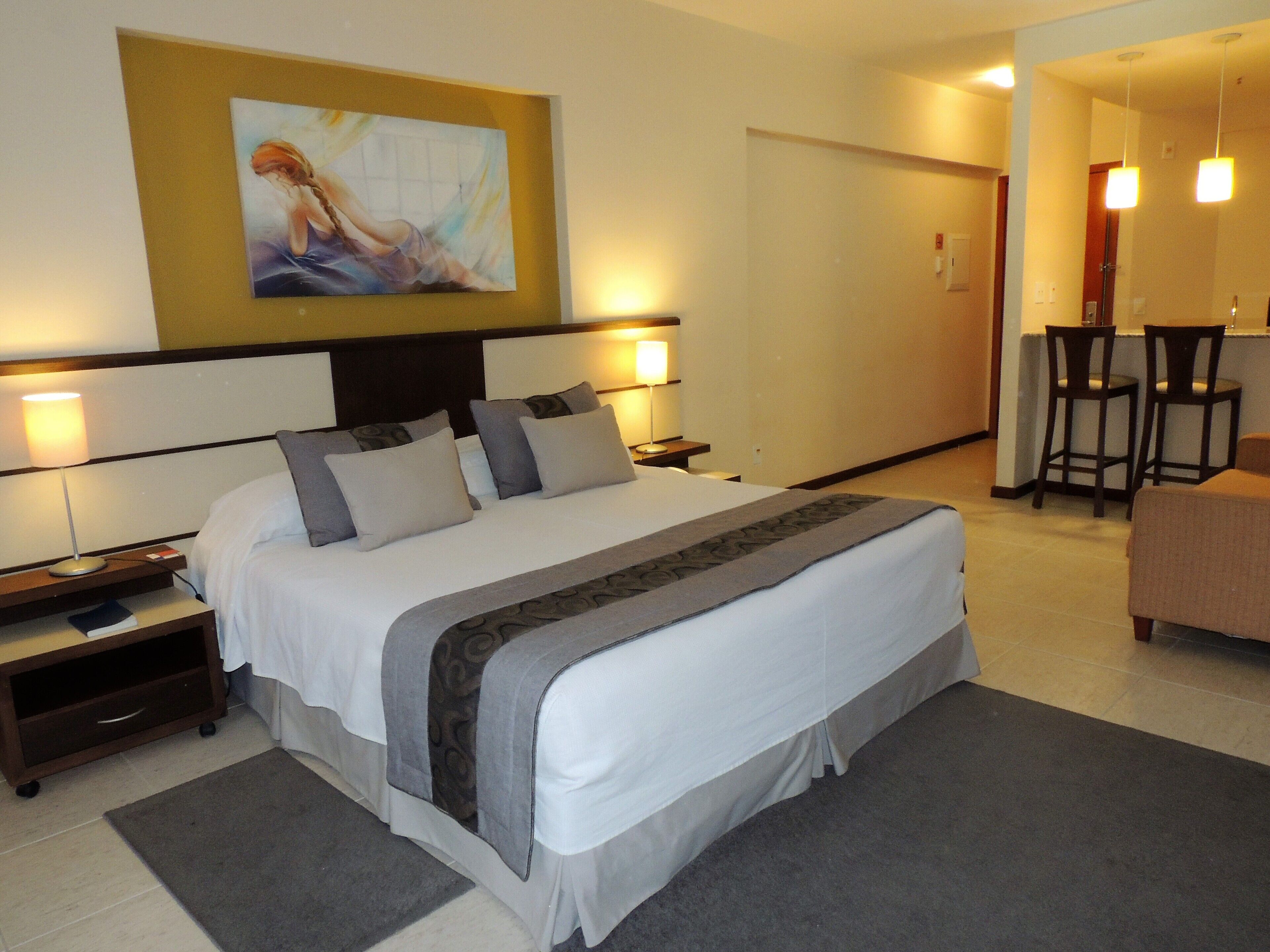 A hotel room with a large bed, two bedside tables, a desk with two chairs, and a painting on the wall.