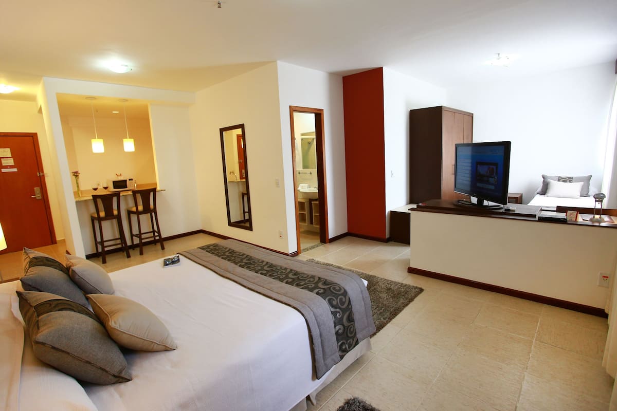Una habitación de hotel con cama, escritorio, televisor y baño visible a través de una puerta abierta.