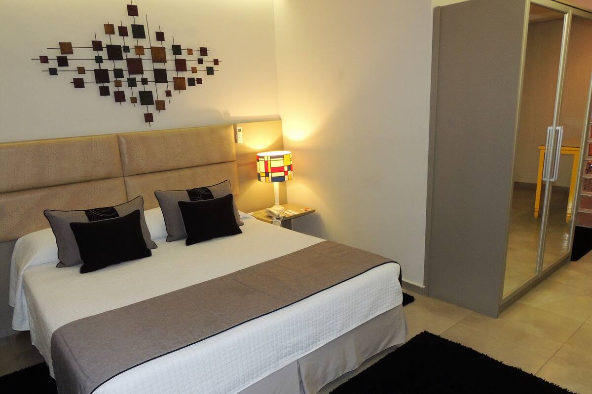 Una habitación de hotel con cama, mesita de noche, lámpara y armario.