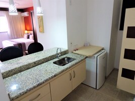 Una cocina compacta con encimera de granito, un lavamanos, un refrigerador y una zona de comedor con una cama al fondo.