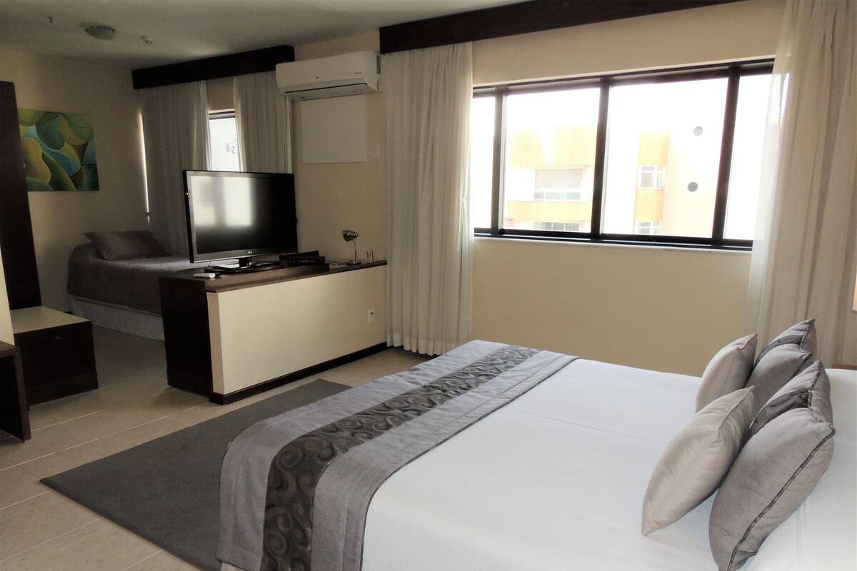 Una habitación de hotel con cama, escritorio, televisor y ventana con cortinas.
