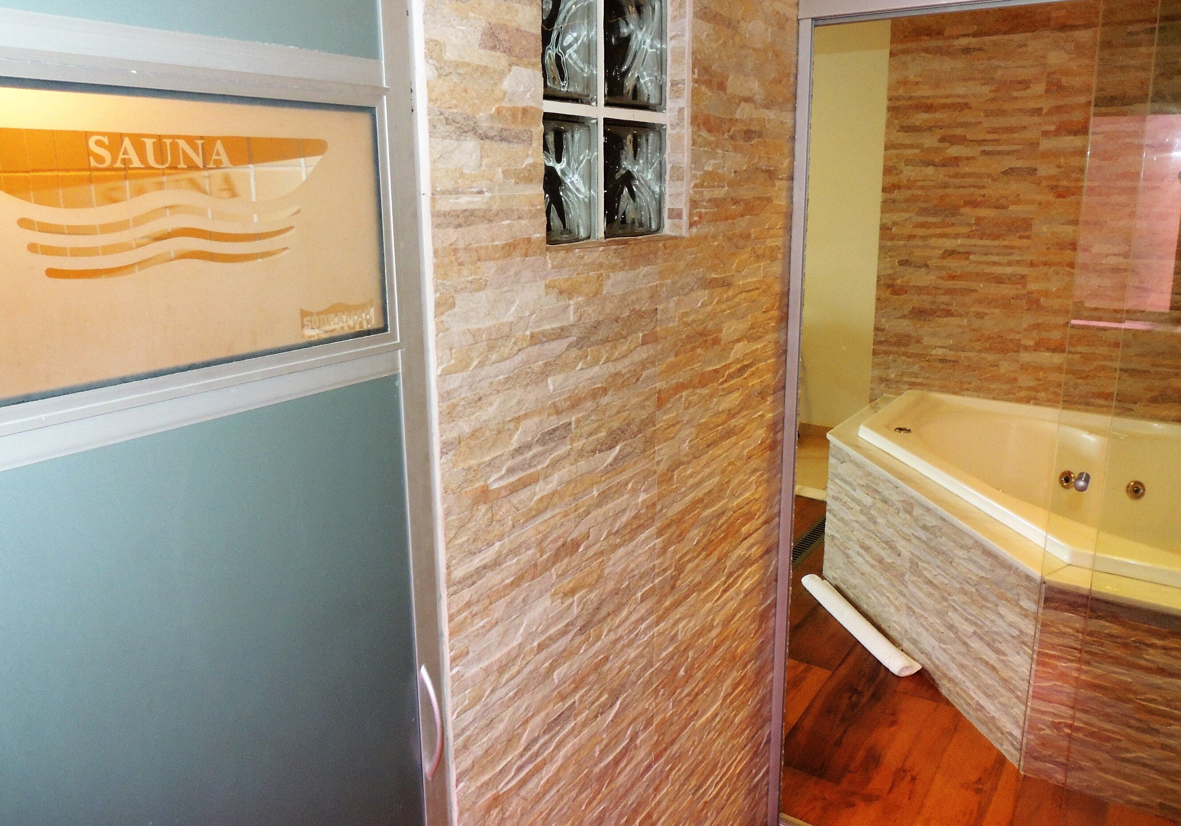 Un baño con pared de piedra, una bañera y un cartel que dice "SAUNA".