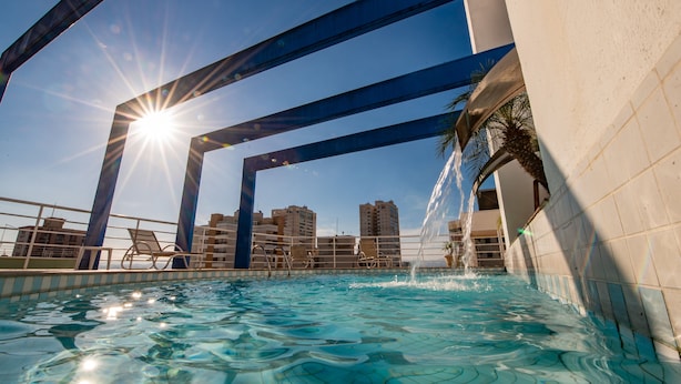 A swimming pool with clear water, a sun shining through the structure, and a cityscape in the background.