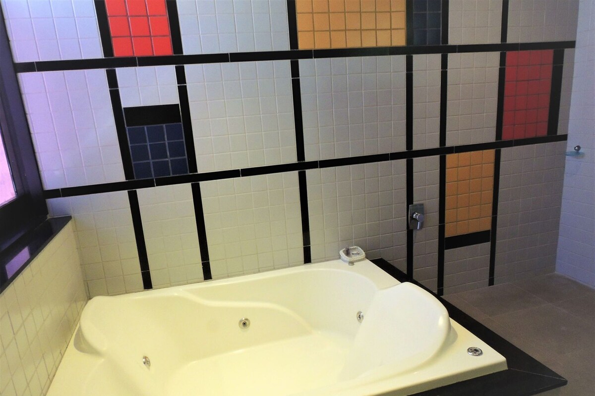 Un baño con una bañera blanca, paredes de azulejos negros y un separador de metal negro.
