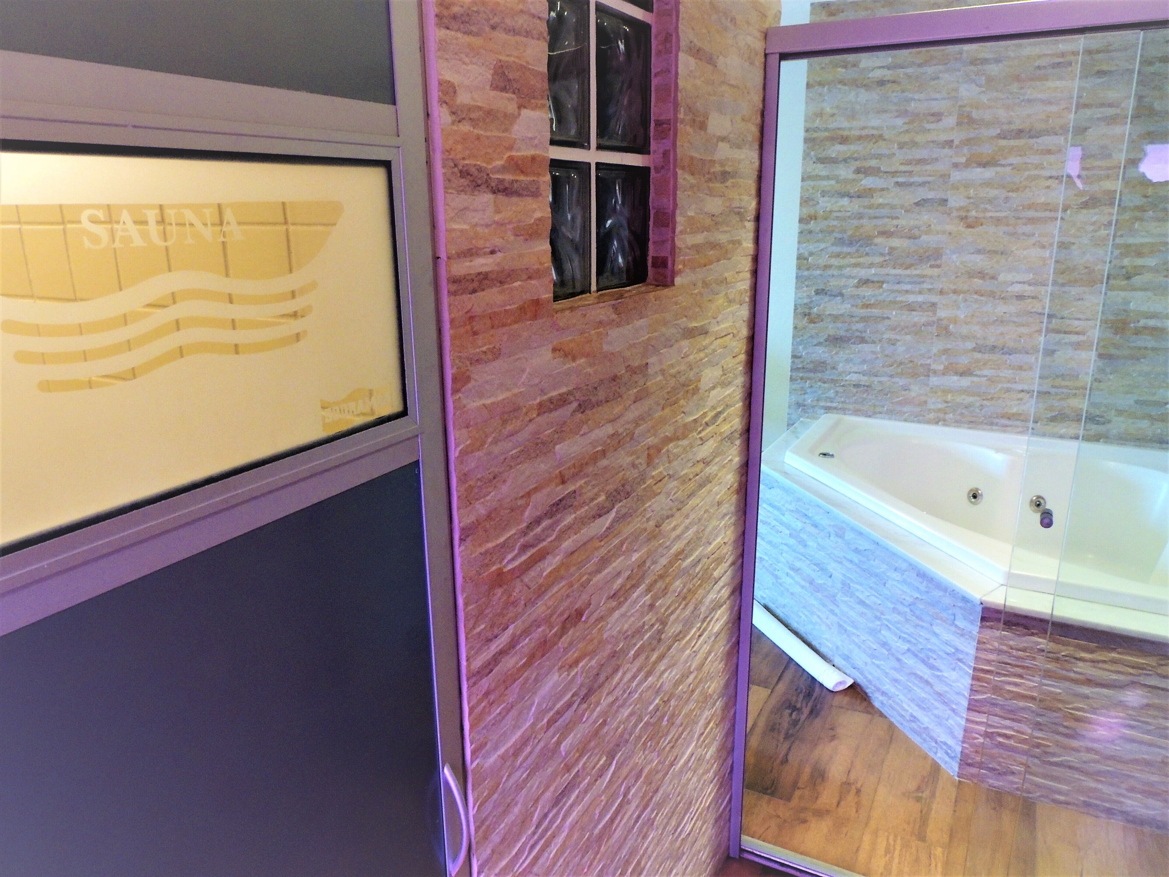 Une salle de bain avec un mur en pierre, une baignoire et un tableau encadré portant l’inscription « SAUNA ».