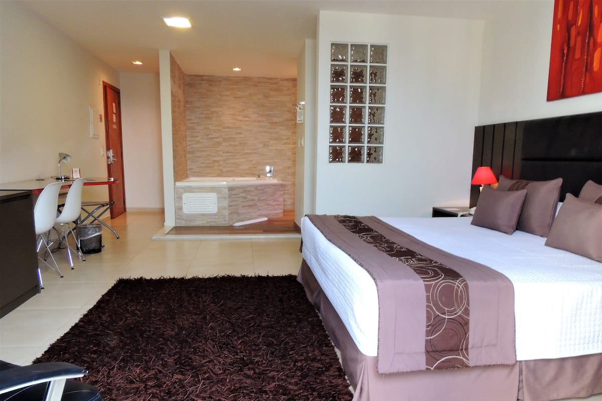 Un dormitorio con una cama grande, un escritorio con sillas, una zona de ducha y un baño.