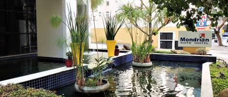 A hotel courtyard with a small water feature, potted plants, and a sign for the Mondrian Suite Hotel.