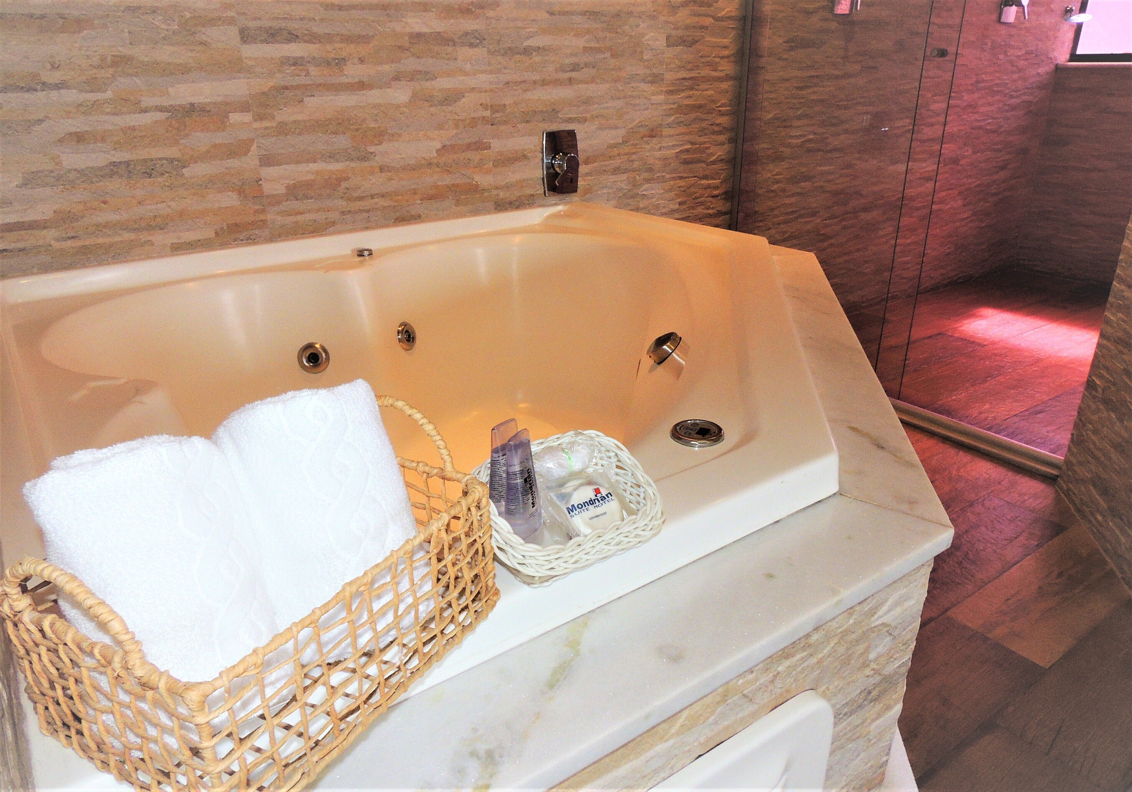 A bathtub with a wicker basket containing a towel and a bottle.