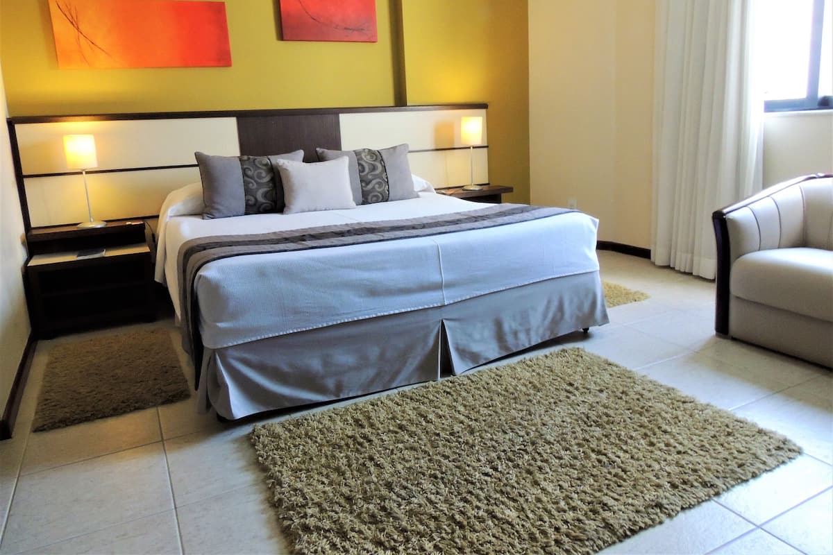 Una habitación de hotel con una cama grande, dos mesitas de noche, una silla y una obra de arte en la pared.
