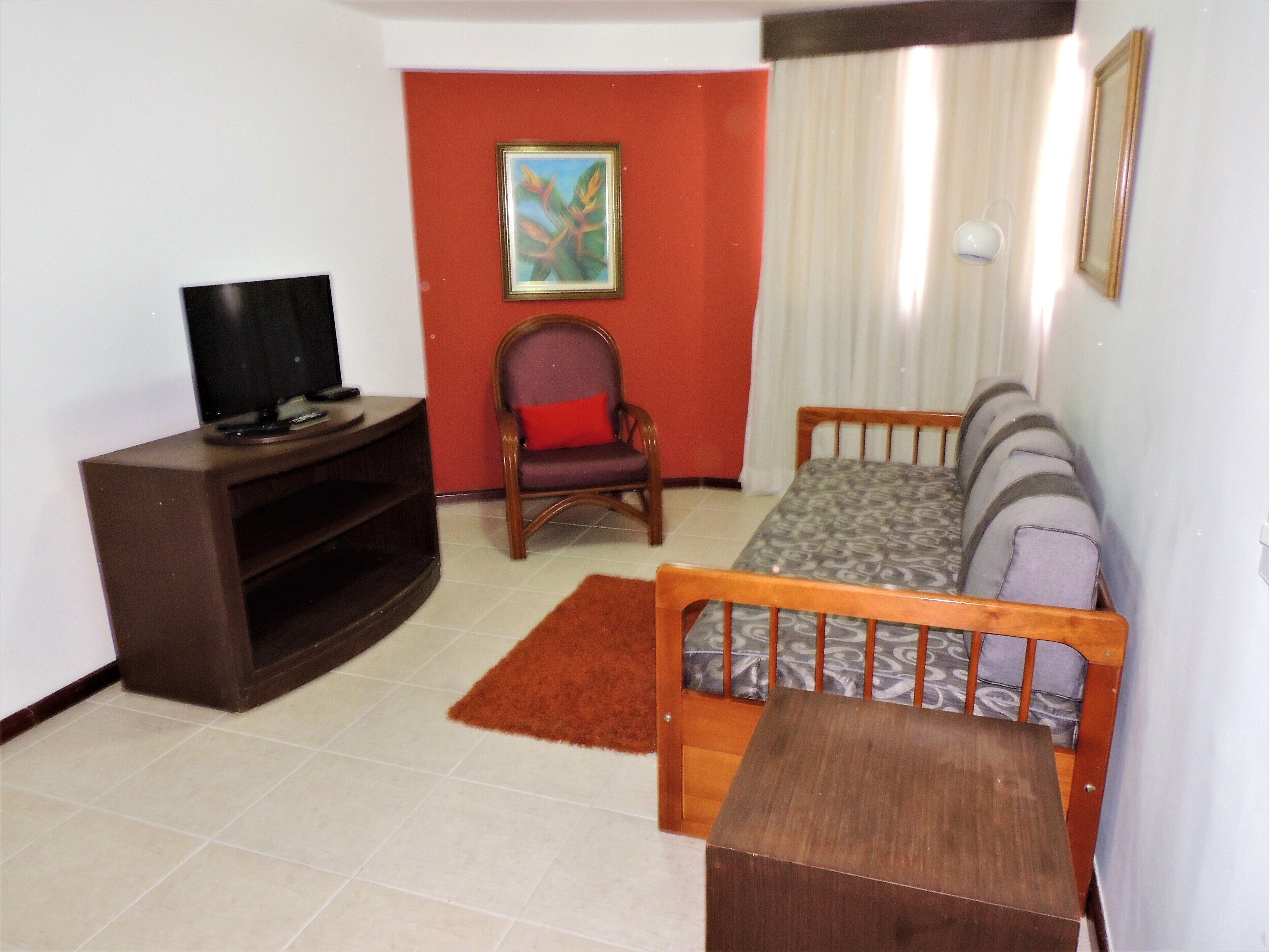 Uma sala de estar com televisão, sofá, poltrona e uma pequena mesa de madeira.