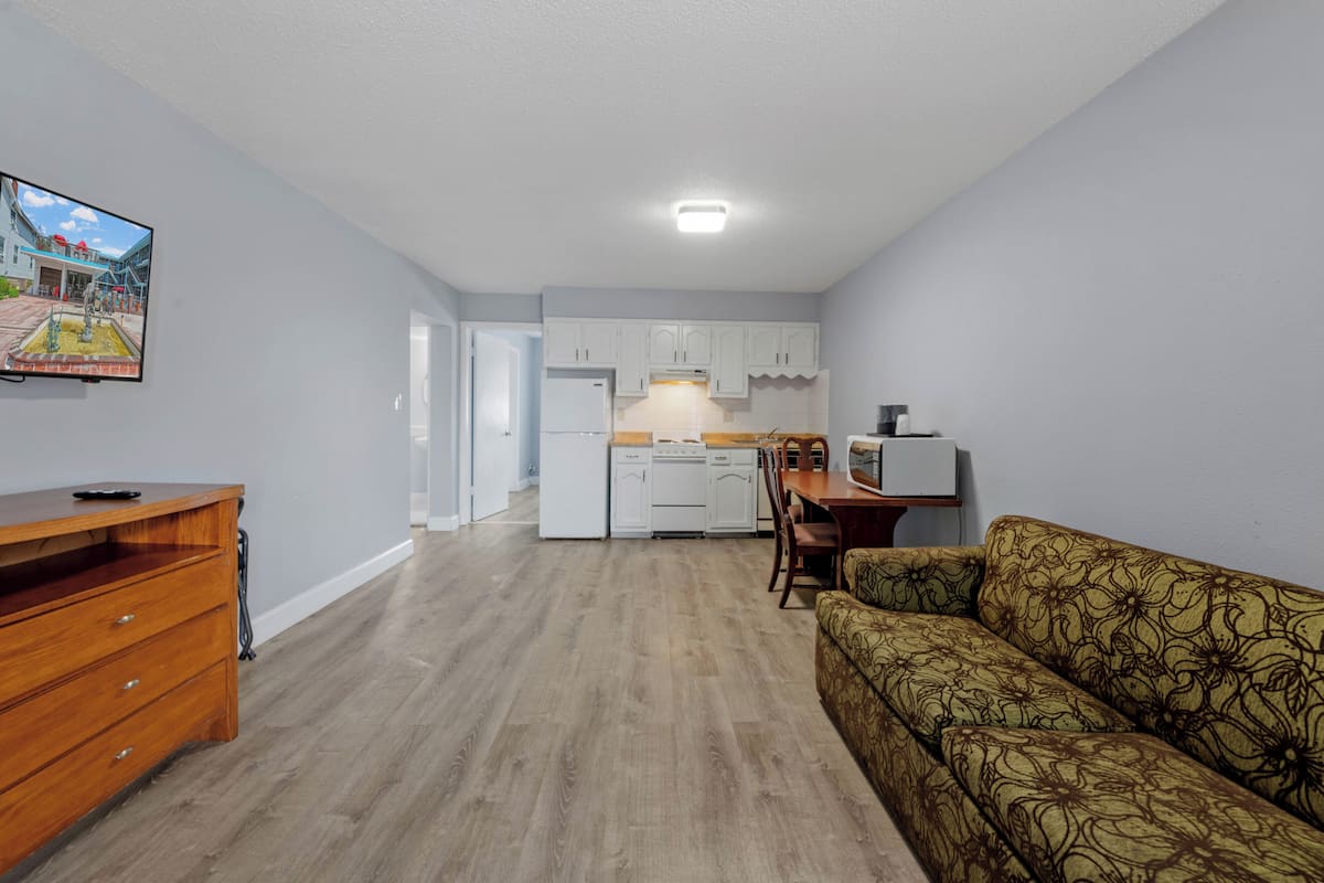 A compact living space with a kitchenette, a sofa, a wooden dresser, and a flat-screen TV mounted on the wall.