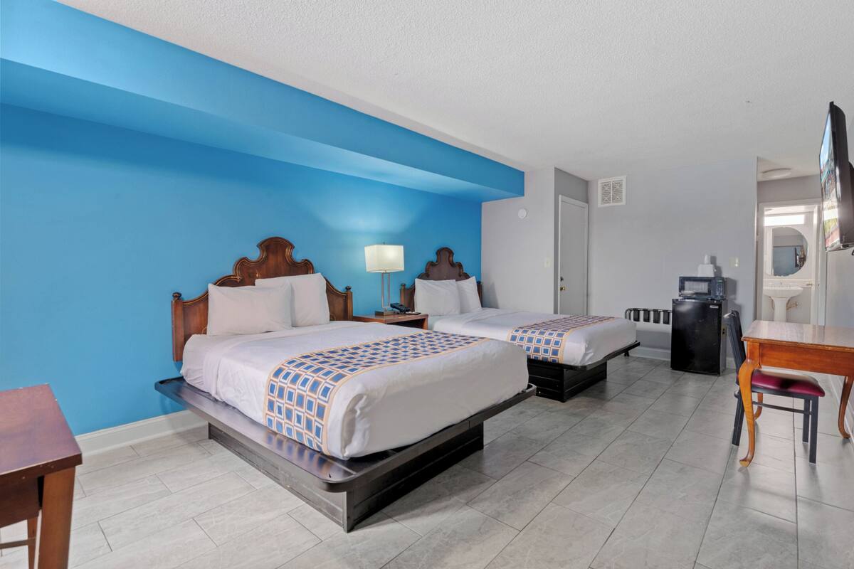 A hotel room with two beds, a desk, a chair, a TV, and a refrigerator.