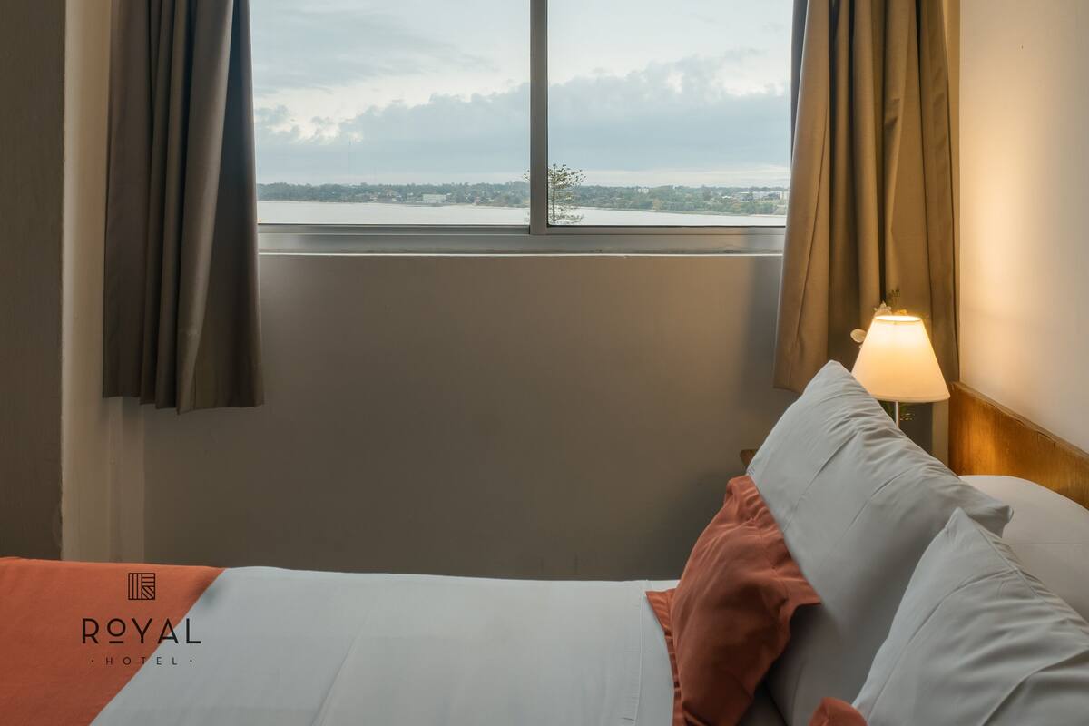 A hotel room with a bed, a window with curtains, and a lamp on the nightstand.