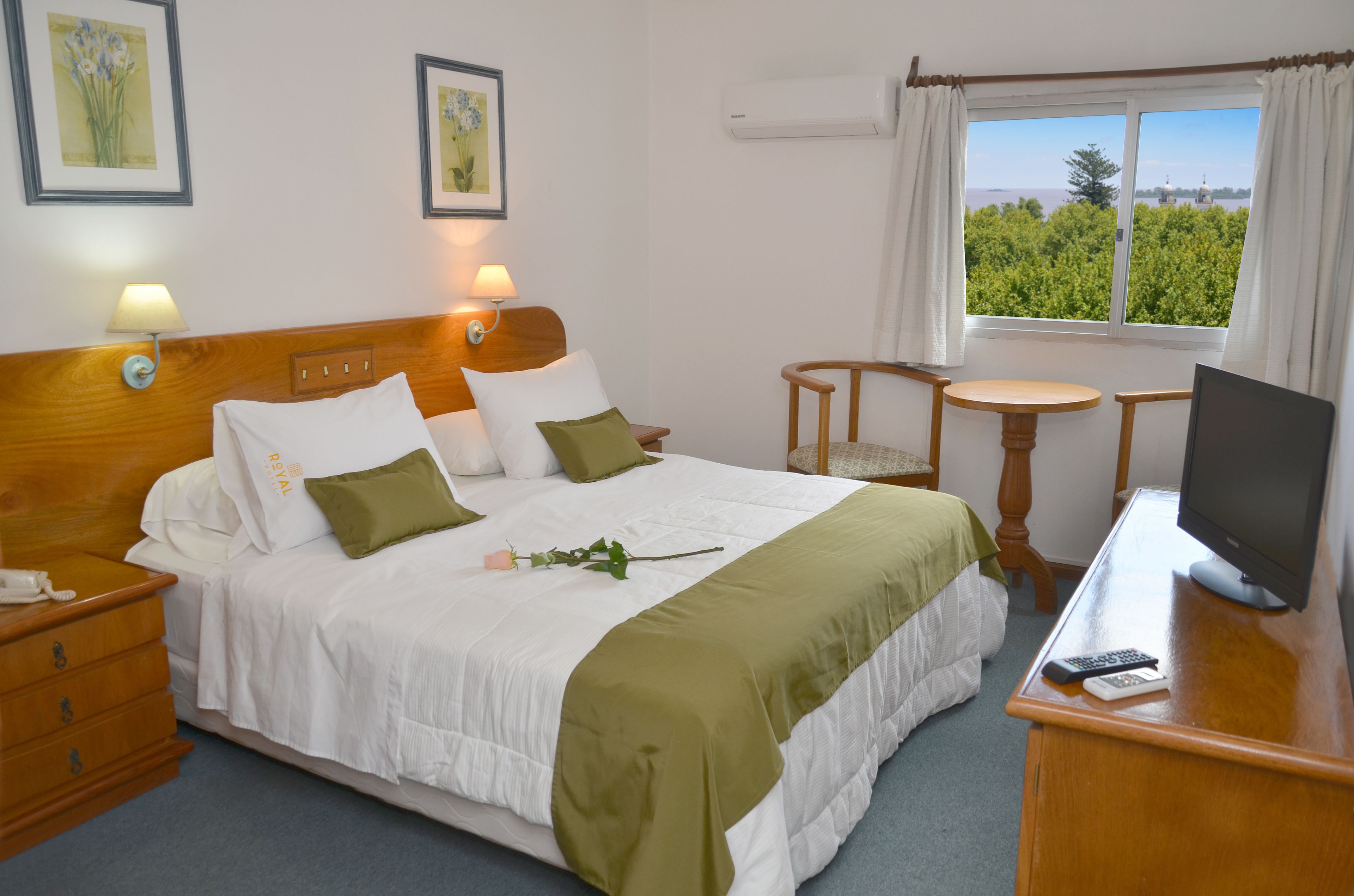 Habitación de hotel con cama, mesitas de noche, televisor, escritorio y ventana con vistas.