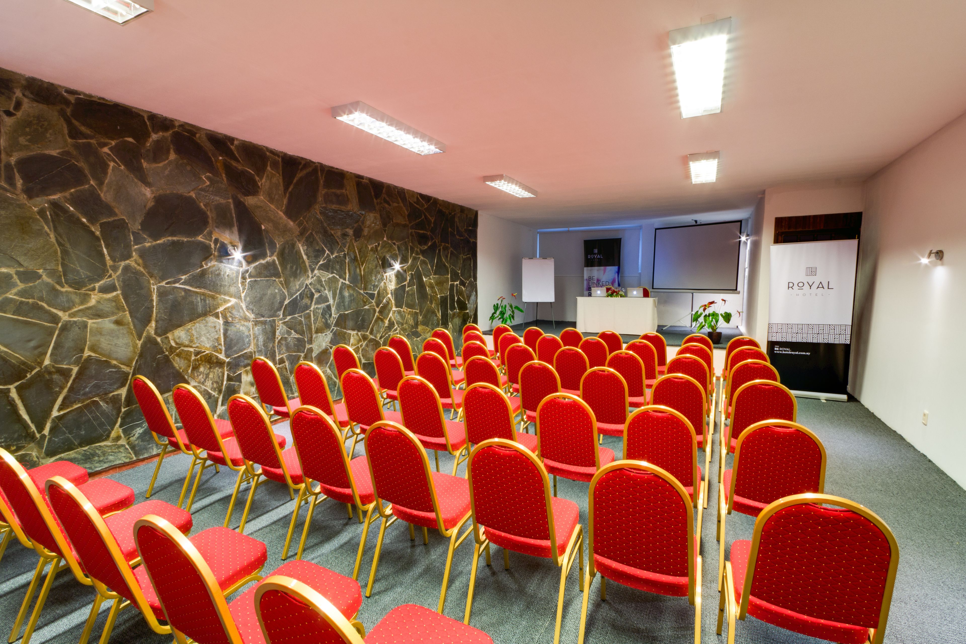 A conference room with rows of red chairs and a stone wall.