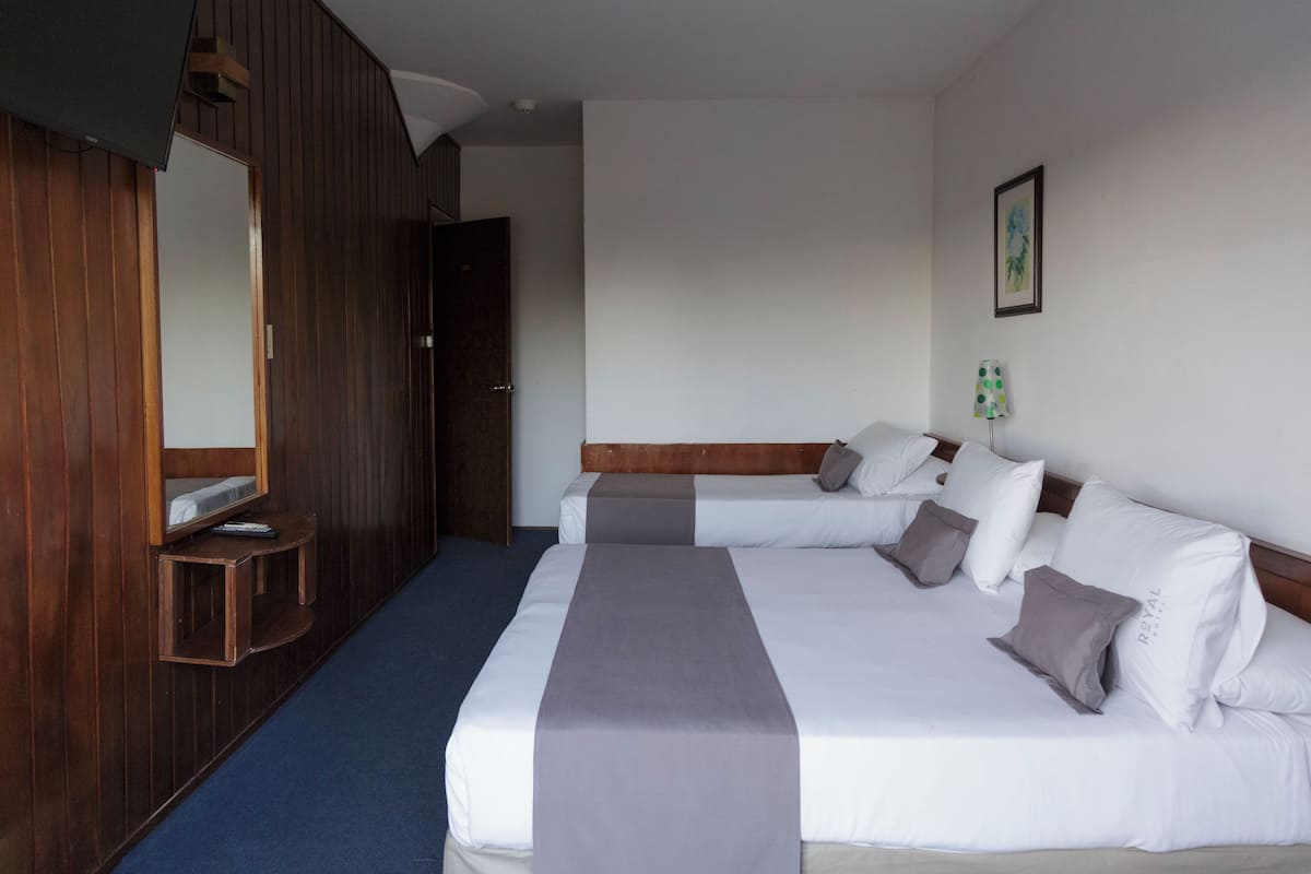 A hotel room with two beds, a wooden wardrobe, a mirror, and a framed picture on the wall.