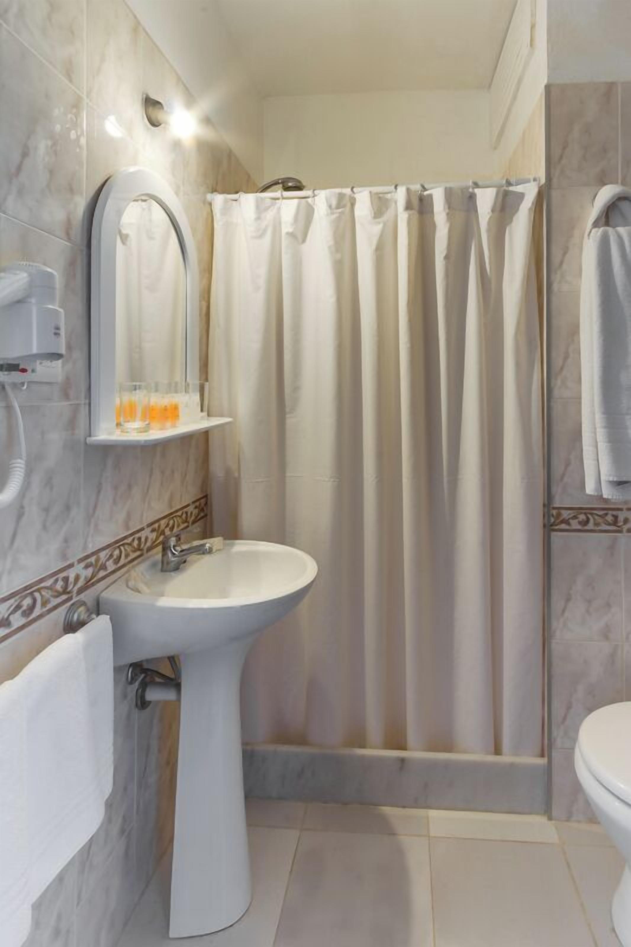 A bathroom with a white sink, a mirror, a shower curtain, and a towel rack.