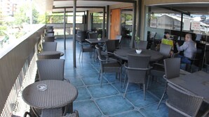 An outdoor patio area with round tables and chairs, a glass wall, and a view of the city. - Cebu R Hotel Mabolo (Cebu City)