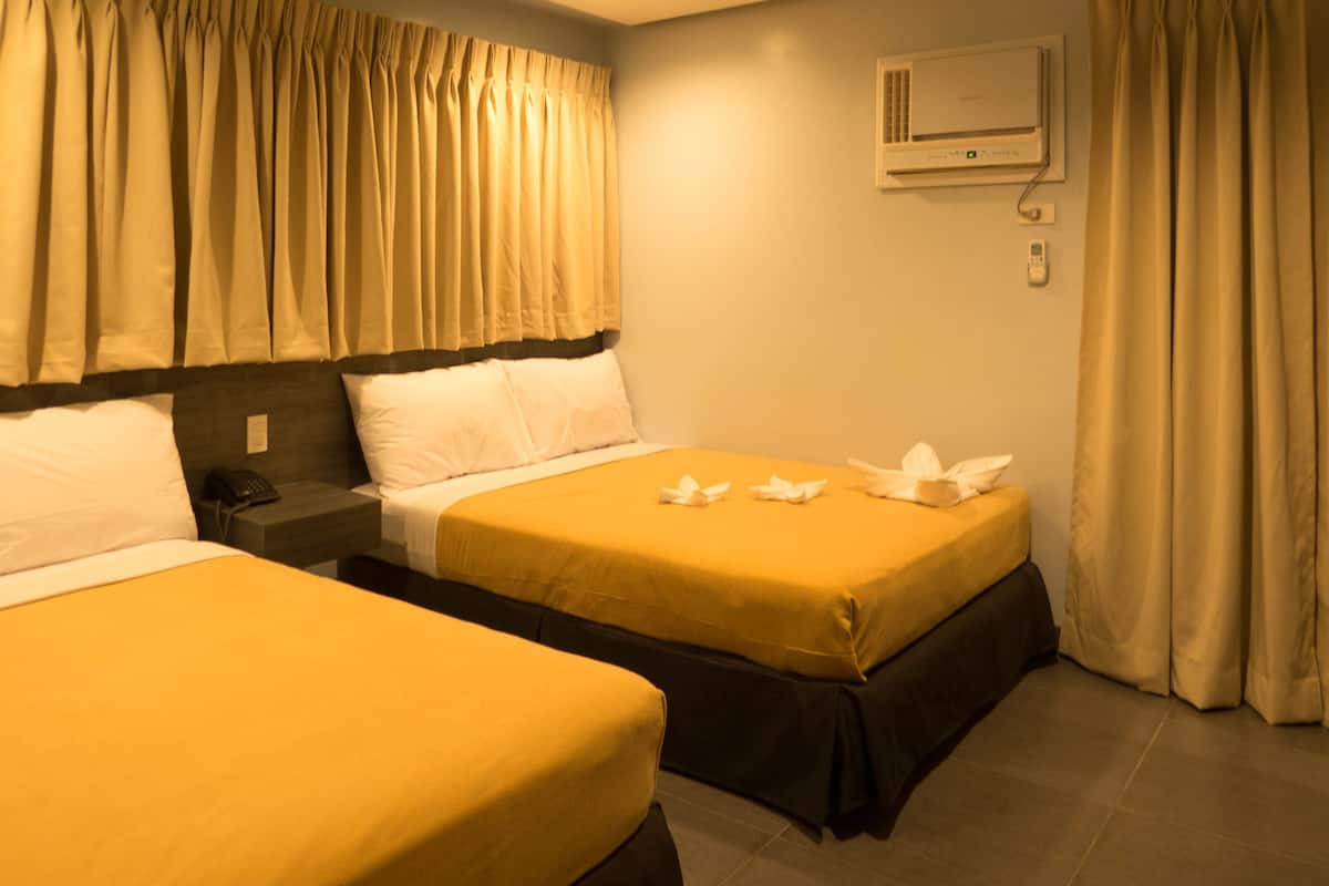 Habitación de hotel con dos camas, cortinas color beige, una mesita de noche con teléfono y aire acondicionado de pared.