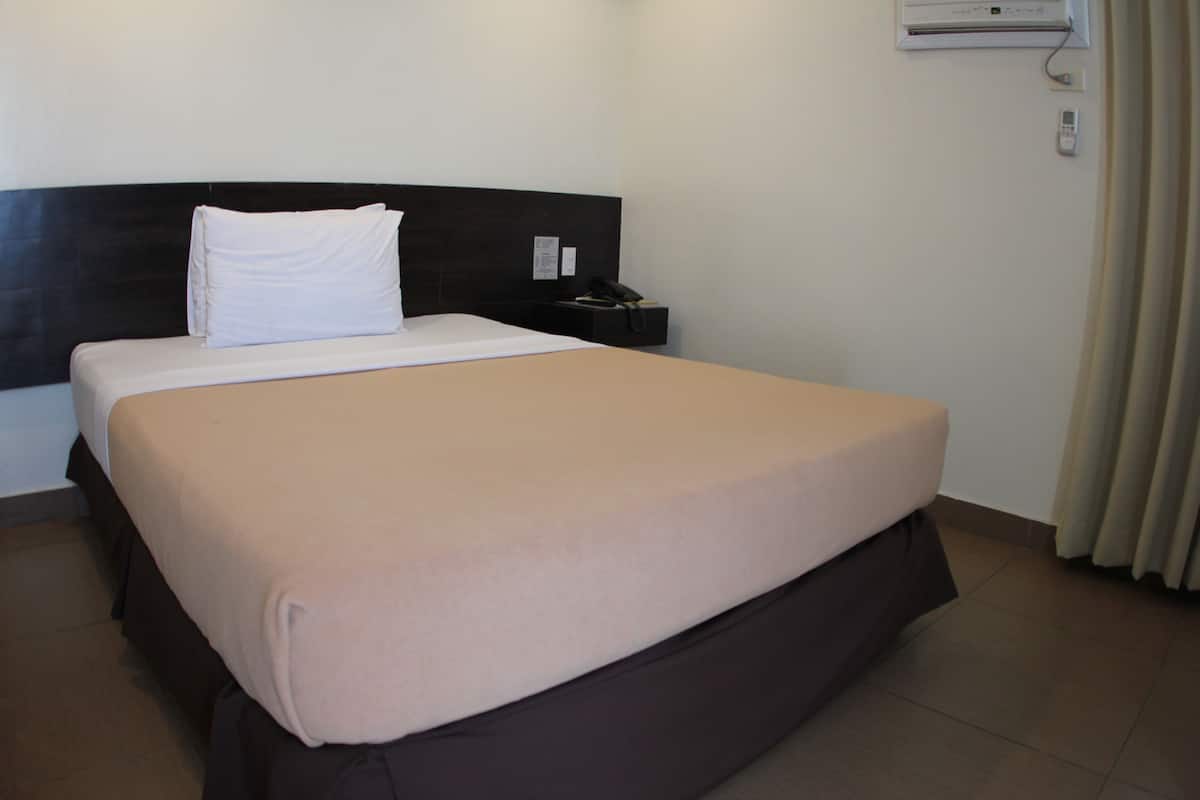 Una cama bien hecha con una almohada blanca y una colcha color beige en una habitación de hotel.