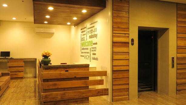 A reception area with a wooden reception desk, a wall with multilingual 'welcome' signs, and an elevator. - Cebu R Hotel Mabolo (Cebu City)