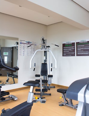 Una palestra con attrezzature per esercizi, uno specchio e manifesti informativi alle pareti.
